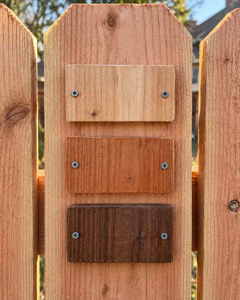 Three stain sample boards screwed to a cedar picket: natural, cedar tone and dark walnut.